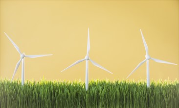 Model wind turbines in grass on yellow background.