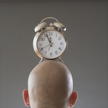 Back view of man with alarm clock on shaved head.