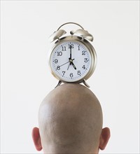 Back view of man with alarm clock on shaved head.