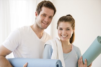Happy young couple posing with exercising mats. Photo : Jamie Grill