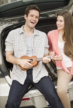 Happy young couple sitting in car boot with mandolin. Photo: Jamie Grill