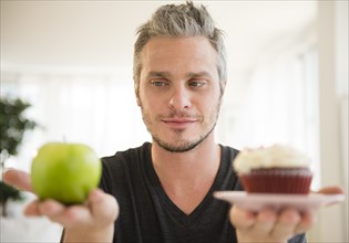 Man weighing green apple against cup cake. Photo: Jamie Grill
