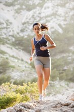 France, Marseille, Young woman jogging on rocky terrain. Photo: Mike Kemp