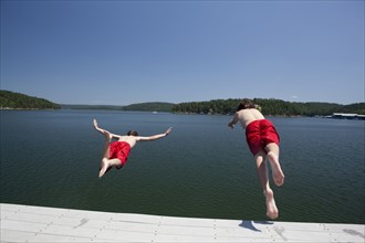 USA, Arkansas, Murfreesboro, Two brothers (8-9, 12-13) jumping into water. Photo: King Lawrence