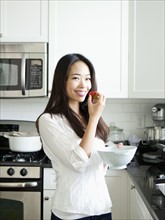 Portrait of smiling young woman eating strawberry in kitchen. Photo : Jessica Peterson