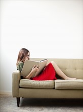 Young woman on sofa reading book. Photo : Jessica Peterson