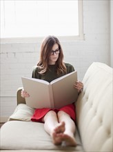 Young woman on sofa reading book. Photo : Jessica Peterson