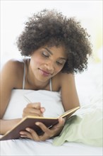 Woman lying on bed writing diary.