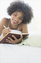 Woman lying on bed writing diary.