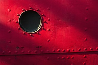 Porthole of red nautical vessel.