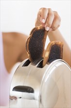 Woman taking burnt toast from toaster.