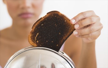 Woman taking burnt toast from toaster.