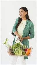 Studio shot of woman holding shopping basket with vegetables.