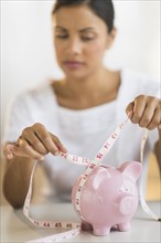 Woman measuring piggy bank.