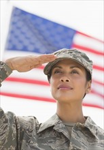 Female army soldier saluting, American flag in background.