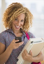 Young woman carrying books and using mobile phone.