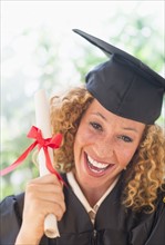 Portrait of smiling young woman in mortarboard showing diploma.