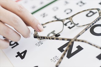 Close up of woman's hands holding glasses above eye chart, studio shot.