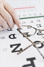 Close up of woman's hands holding glasses above eye chart, studio shot.