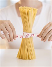 Close up of woman's hands measuring pasta with tape measure.