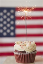 Studio shot of sparkler atop cupcake, american flag in background. Photo : Jamie Grill