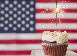 Studio shot of sparkler atop cupcake, american flag in background. Photo: Jamie Grill