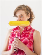 Studio shot of young woman holding paint roller. Photo: Daniel Grill
