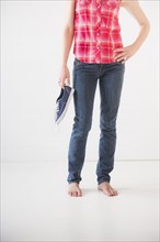 Studio shot of young barefoot woman holding shoes, low section. Photo: Daniel Grill