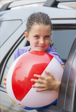 Young girl (8-9) with beach ball peeking through car window . Photo: Daniel Grill
