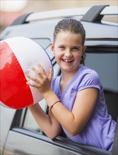 Young girl (8-9) with beach ball peeking through car window . Photo : Daniel Grill