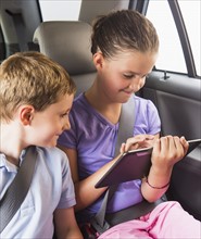 Boy (6-7) and girl (8-9) using digital tablet while sitting in car. Photo : Daniel Grill