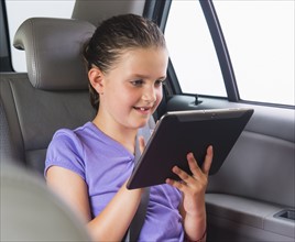 Girl (8-9) using digital tablet while sitting in car. Photo : Daniel Grill