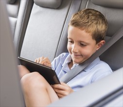 Boy (6-7) using digital tablet while sitting in car. Photo : Daniel Grill