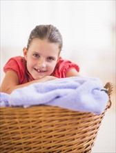 Young girl (8-9) leaning on laundry basket. Photo : Daniel Grill