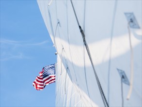 White sails and American flag against blue sky. Photo : Daniel Grill