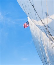 White sails and American flag against blue sky. Photo: Daniel Grill