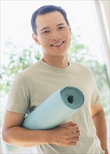 Happy mid adult man holding exercising mat. Photo : Daniel Grill