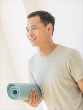 Happy mid adult man holding exercising mat. Photo : Daniel Grill