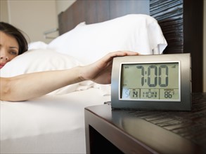 Young attractive woman turning off alarm clock.