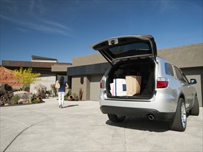 Young woman unpacking shopping from car parked in yard. Photo: Erik Isakson