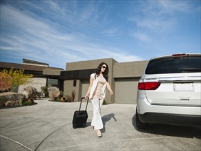 Young woman with suitcase walking towards car.