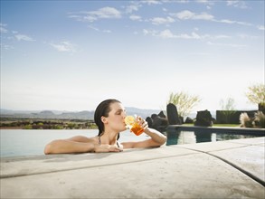 Young attractive woman enjoying cocktail on edge of swimming pool.