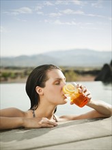 Young attractive woman enjoying cocktail on edge of swimming pool.
