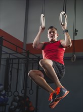 Mature man doing pull-ups with acrobatic rings.