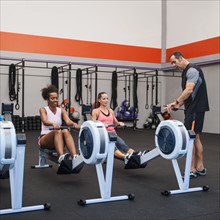 Two women exercising in gym supervised by their trainer.