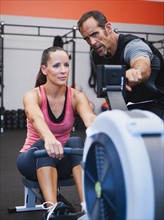 Woman exercising on row machine supervised by her trainer.