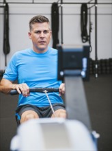 Mature man exercising on row machine in gym.