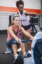 Woman exercising on row machine supervised by her trainer.