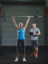 woman lifting barbell supervised with her trainer.