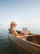 Young woman relaxing in canoe, and reading book.